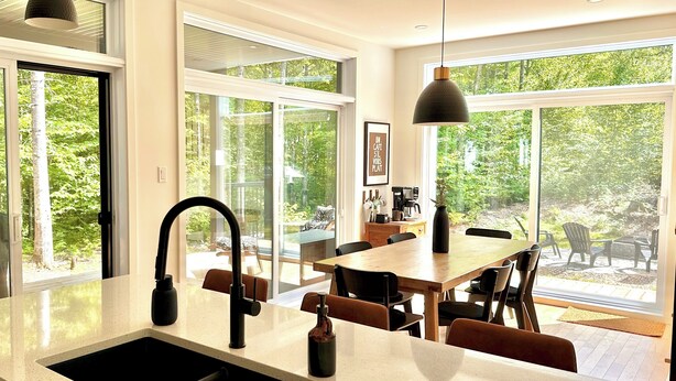 Een moderne keuken met een groot eiland, hangende lampen en grote ramen met uitzicht op de omgeving.