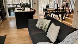 A modern living room with a dark-colored sofa, a small coffee table, and a kitchen area in the background. - Modern chalet 2 minutes from the Bras-du-Nord Valley | Spa & Sauna  (Saint-Raymond)