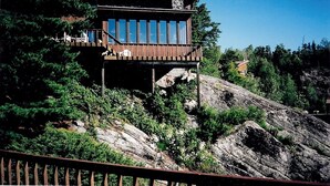 Une cabane en bois dotée d’un balcon, entourée d’arbres et d’un paysage rocheux.