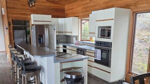 Une cuisine moderne avec un plafond en bois, des appareils en acier inoxydable et un coin bar avec des tabourets.