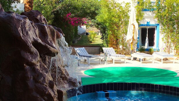 Un área de piscina con cascada, sillas de descanso y una piscina pequeña.
