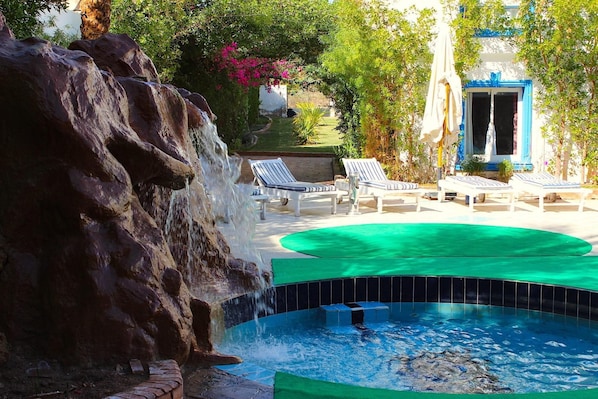 Un espace piscine agrémenté d’une cascade, de chaises longues et d’une petite piscine.