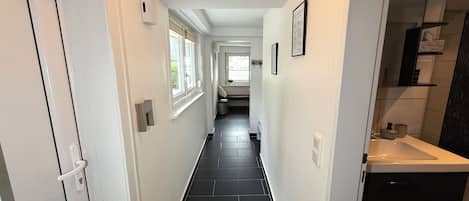 A hallway with black tiled flooring, white walls, and a bathroom with a dark tiled shower area.