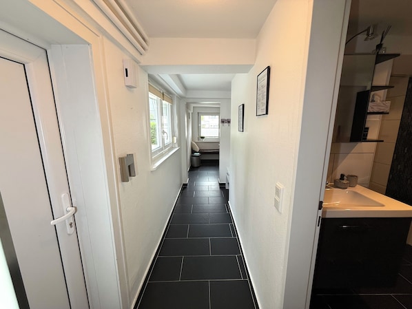 A hallway with black tiled flooring, white walls, and a bathroom with a dark tiled shower area. - PrimeLoft Hirsch - cozy & spacious - private entrance & parking - 84 m² first floor (Braunlage)