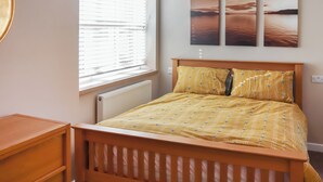 Een slaapkamer met een houten bed, een nachtkastje, een radiator en een raam met jaloezieën.