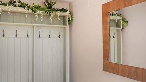 Een witte kast met meerdere haken, een houten bankje en een spiegel met houten lijst.