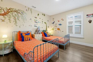 A children's room with two beds, a window with blinds, and dinosaur-themed wall decals.