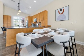 A modern kitchen with wooden cabinets, a central island, and a dining area with a dark wooden table and white chairs.