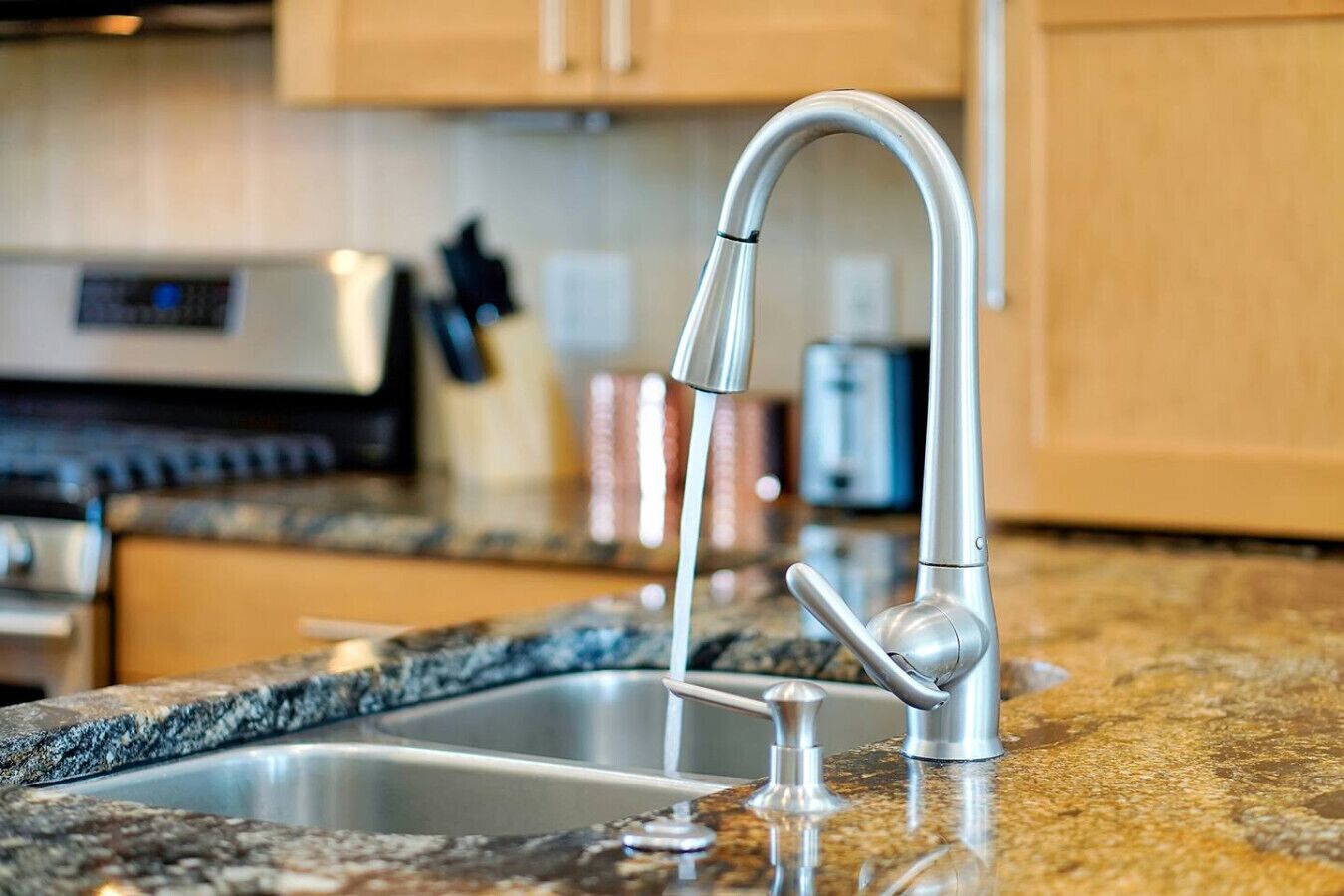 A kitchen with a stainless steel sink, a modern faucet, and granite countertops.