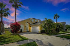 A residential house with a garage, surrounded by well-maintained lawns and palm trees.