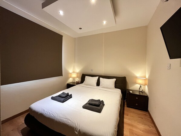 A modern hotel room with a large bed, two bedside tables with lamps, a flat-screen TV mounted on the wall, and a large window.