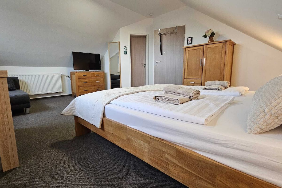 A bedroom with a bed, wooden wardrobe, a television, a radiator, and a door.