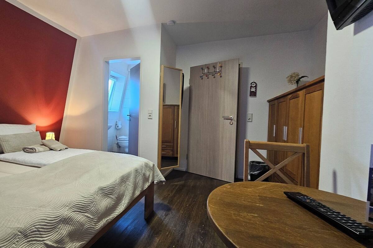 A hotel room with a bed, a wooden nightstand, a TV, and a bathroom visible through an open door.