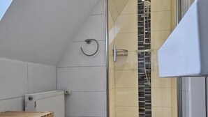 A modern bathroom with a glass shower enclosure, a wooden bench, and a radiator. - Mondlicht Norddeich (Norden)