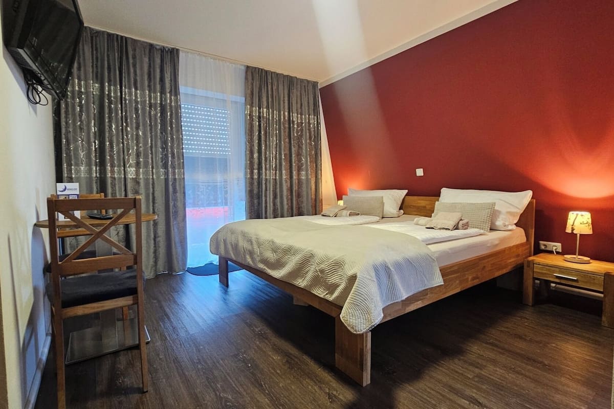 A hotel room with a bed, a desk, a chair, a TV, and a window with curtains.