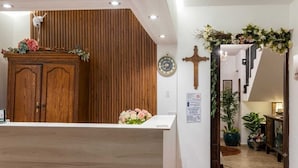 A reception area with a wooden reception desk, a clock, and a cross on the wall. - Suites Madero San Benito (San Salvador)