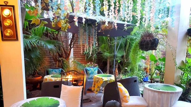 An outdoor patio area with round tables and chairs, surrounded by lush greenery and hanging flowers. - Suites Madero San Benito (San Salvador)