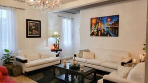Un salon avec deux canapés blancs, une table basse, un lustre, un tableau et une lampe.