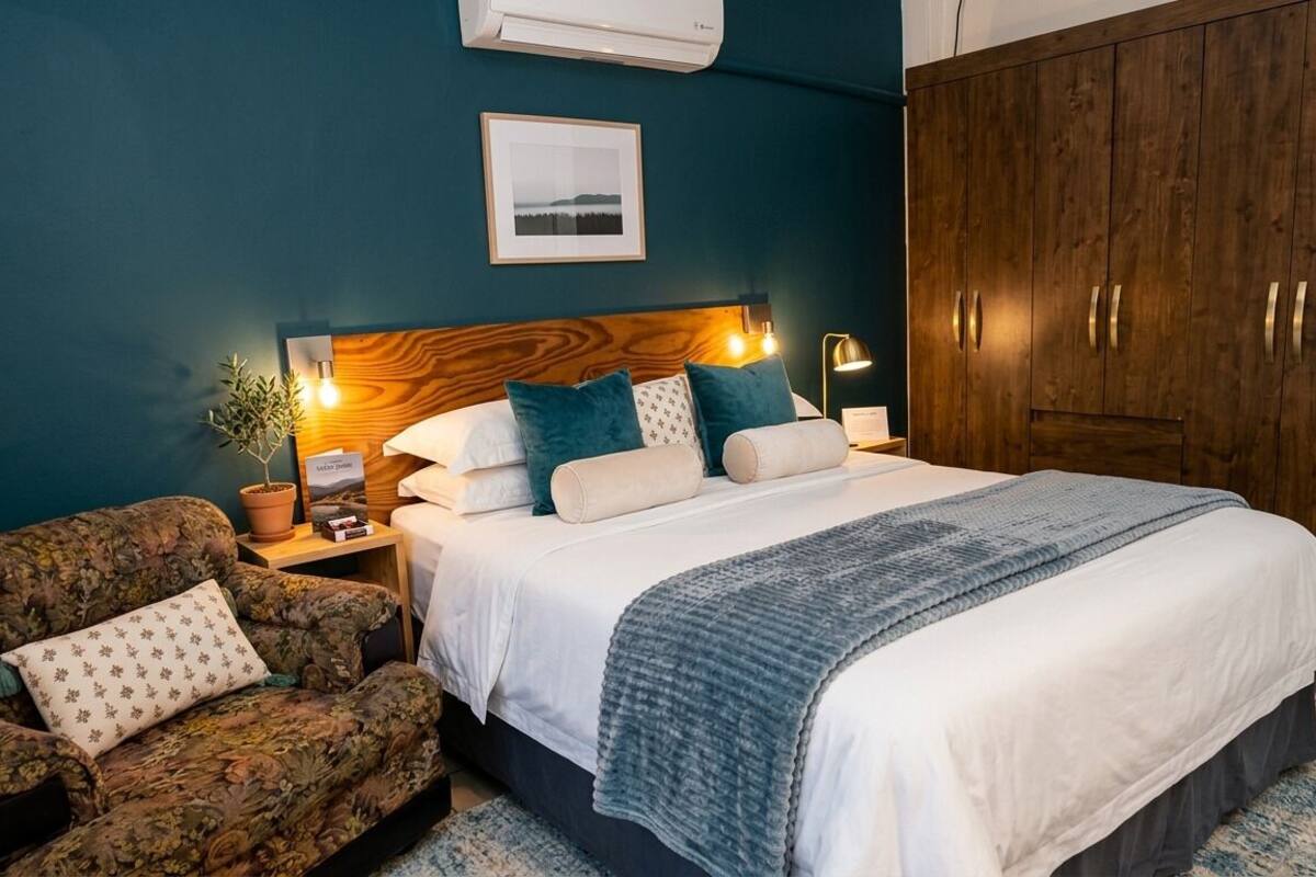 A bedroom with a bed, a nightstand, a lamp, a potted plant, a sofa, and a wardrobe.