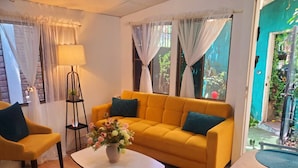 A living room with a yellow sofa, a coffee table with a vase of flowers, and a lamp. - Suites Madero San Benito (San Salvador)