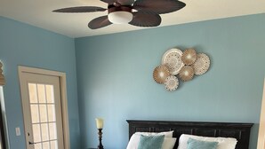 A bedroom with a dark wooden bed, a ceiling fan, and a decorative wall piece.