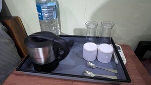 Un plateau avec une bouilloire, deux tasses, une bouteille d’eau et une cuillère, posé sur une table en bois.