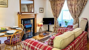 A cozy living room with a fireplace, a television, and a sofa with plaid covers. - The Old Baron's Courthouse (Ceres, near St Andrews)