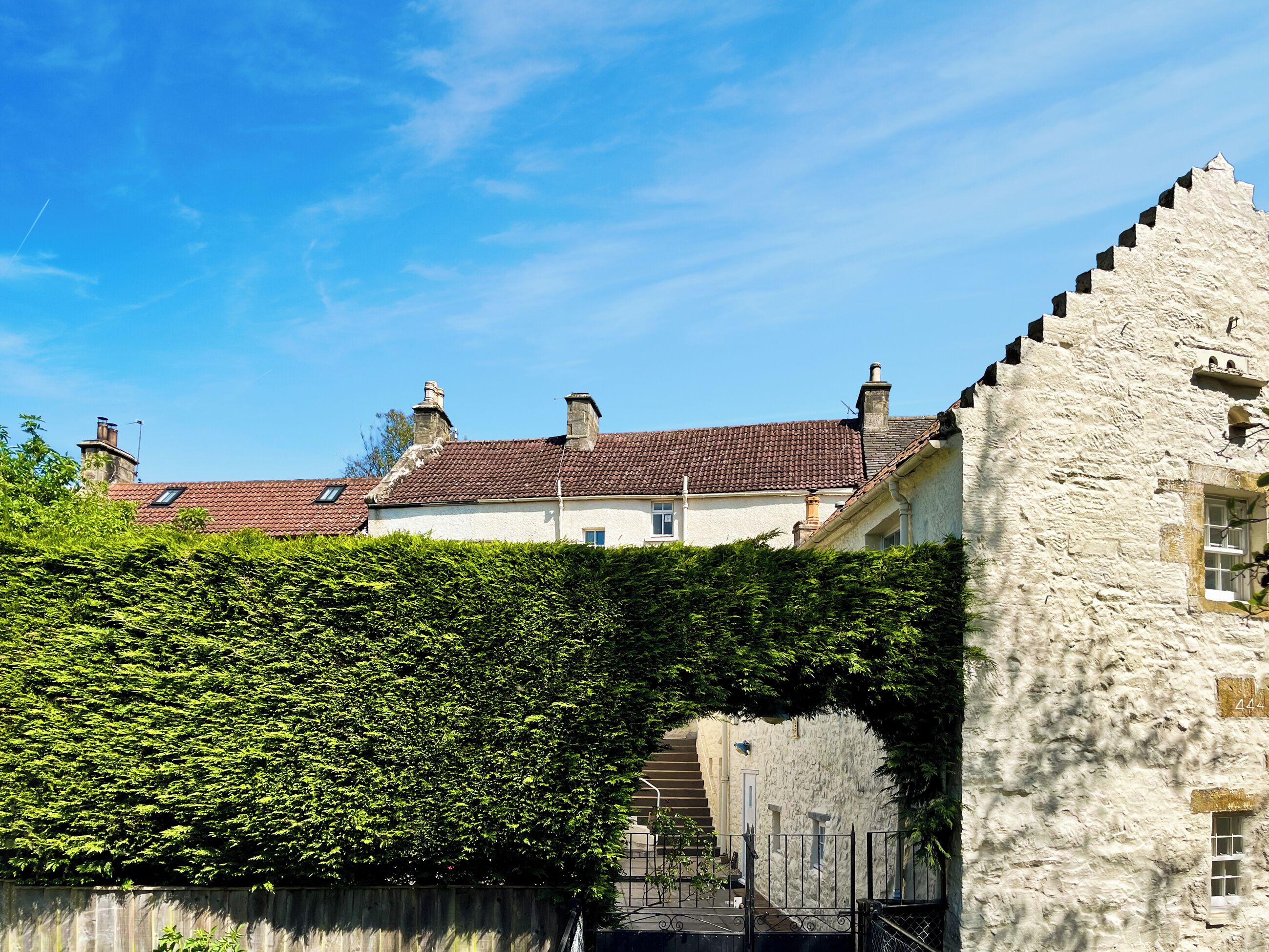 A stone building with a red-tiled roof, a wooden fence, and a well-maintained hedge.