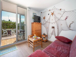 A living room with a red sofa, a wooden cabinet, a television, and a net decoration on the wall. - Apartment in Agde for Four Guests (Agde)