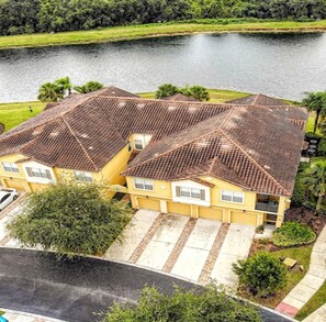 A yellow building with a tiled roof, a driveway, and a body of water in the background.