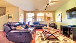 A living room with a brown leather sofa, a glass coffee table, and a television on the wall. - Disney 3BR Home, Pool, Lake View (Kissimmee)