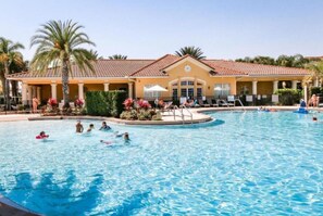 A swimming pool area with a building in the background, palm trees, and people swimming. - Disney 3BR Home, Pool, Lake View (Kissimmee)