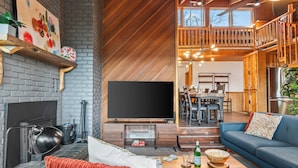 A modern living room with a fireplace, a flat-screen TV, and a dining area visible through an open door.