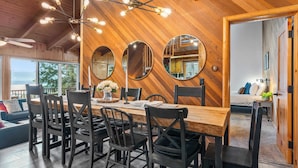 A dining area with a wooden table, black chairs, and a chandelier. There are three round mirrors on the wall and a ceiling fan.