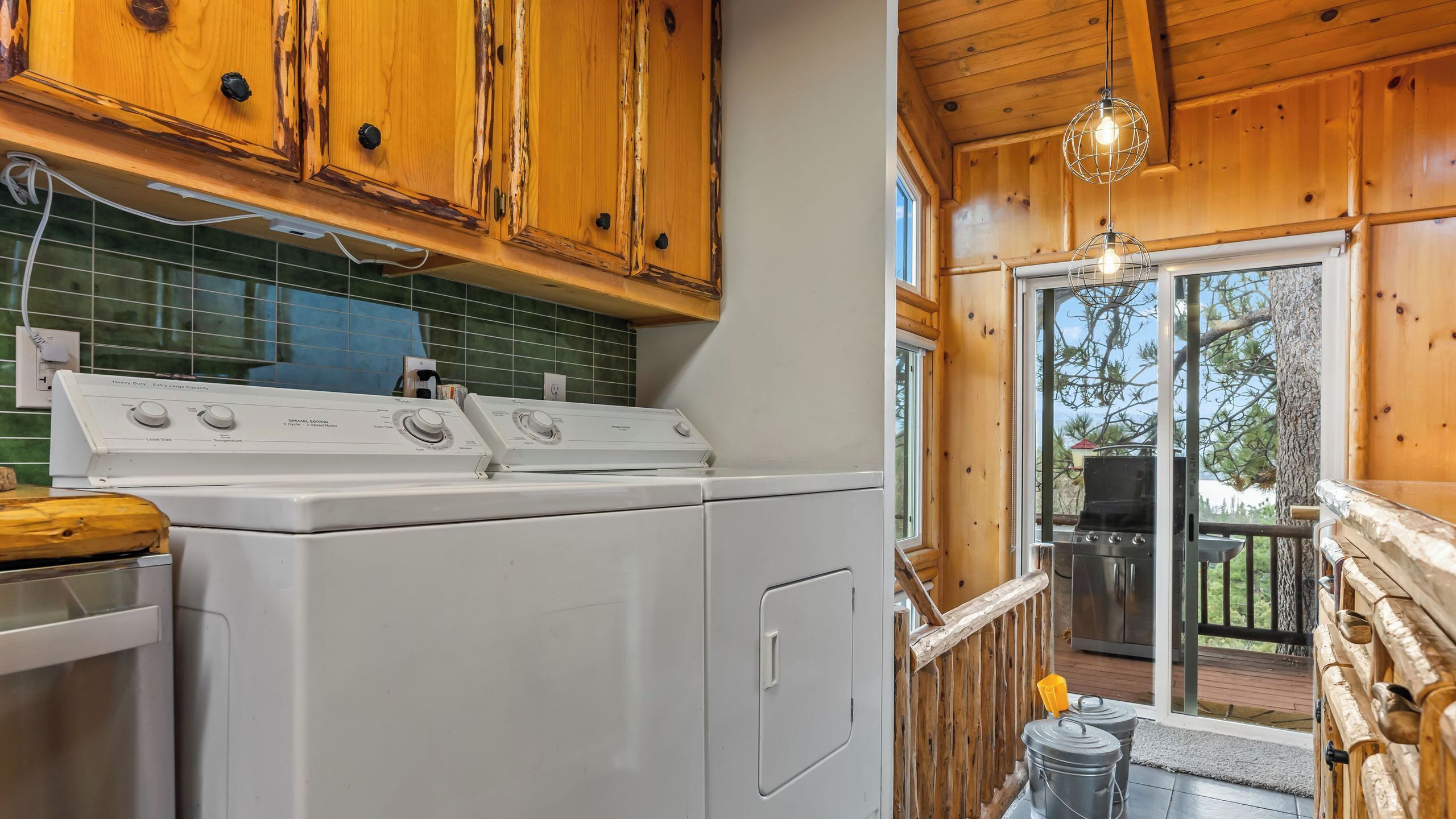 A kitchen with a stove, a washing machine, wooden cabinets, and a view of the outdoors.