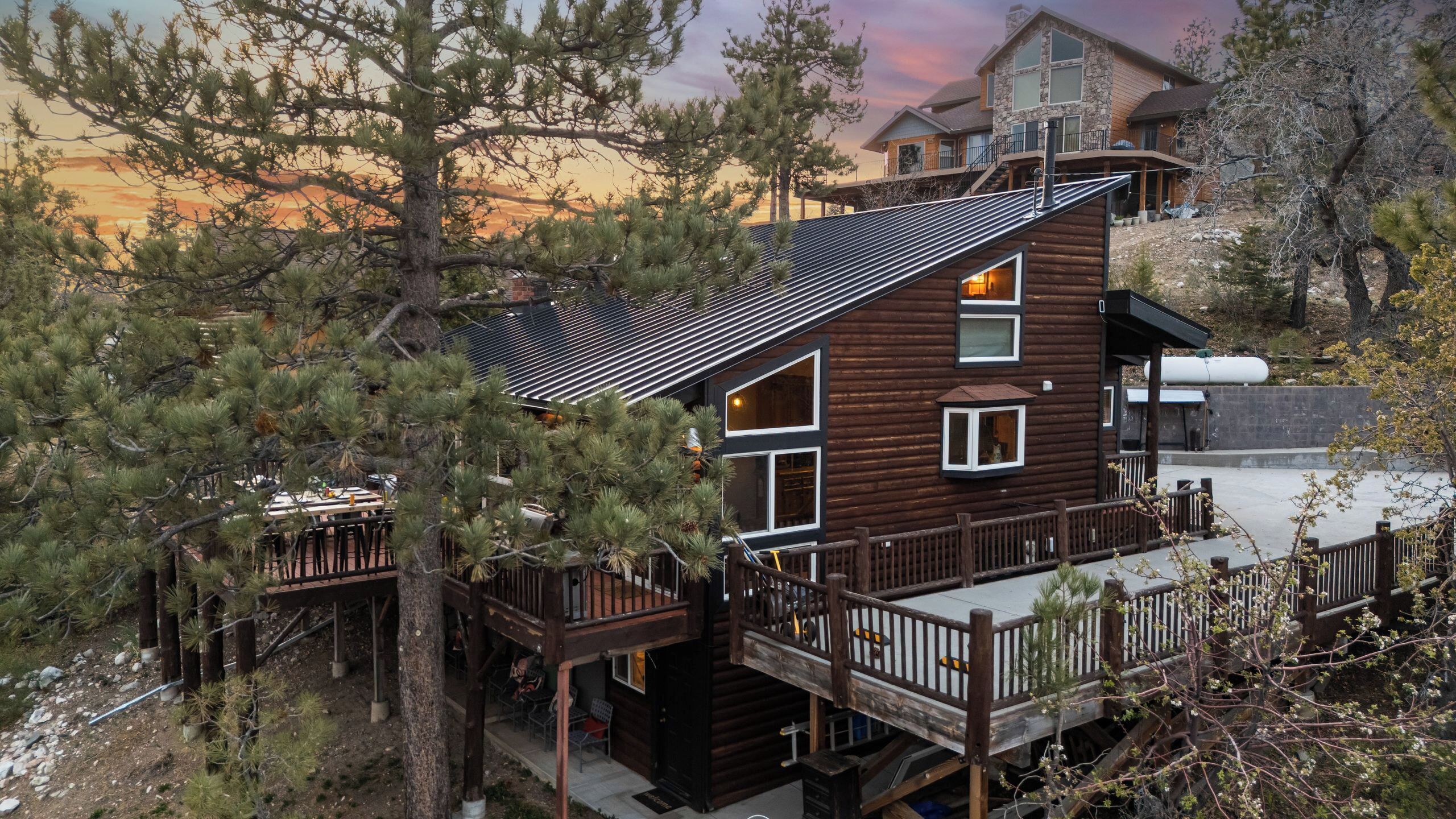 Une cabane en rondins à plusieurs étages, dotée d’un balcon et entourée d’arbres.