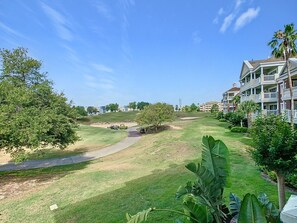A golf course with a pathway, palm trees, and a building with multiple balconies.