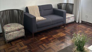 A living room with a dark blue sofa, two patterned armchairs, a framed picture on the wall, and a wooden floor.