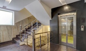 A modern interior with a marble staircase, a glass elevator, and a view of a green outdoor area. - Treebo Trend Hotel NV (Narendranagar)