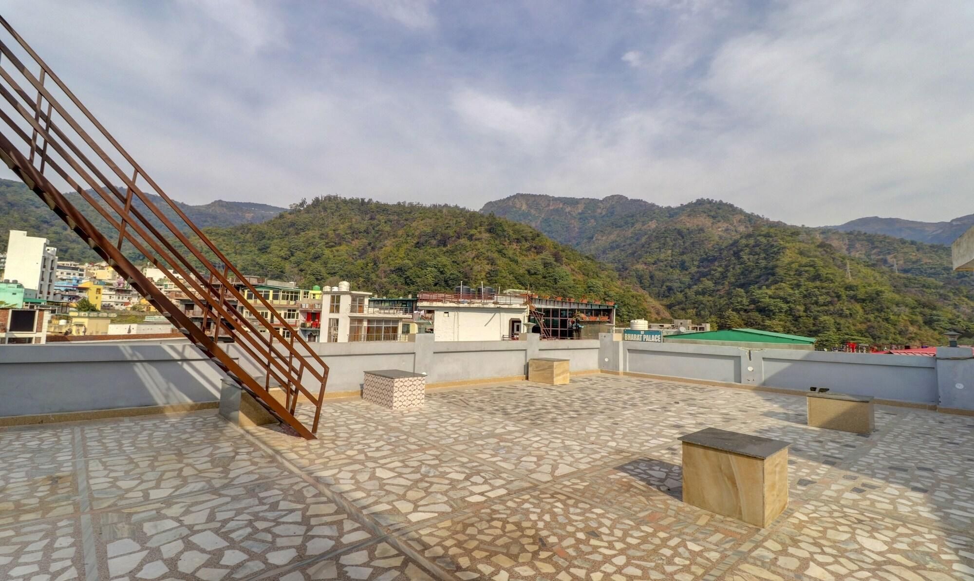 A rooftop terrace with a patterned tile floor, a metal staircase, and a view of a green hillside with buildings in the background.