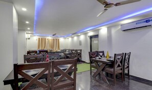 A dining area with tables and chairs, a ceiling fan, and an air conditioning unit. - Treebo Trend Hotel NV (Narendranagar)