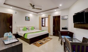 A hotel room with a bed, bedside table, TV, and a desk with a chair. - Treebo Trend Hotel NV (Narendranagar)