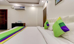A hotel room with a bed, pillows, a bedside table with a water bottle, a clock, and an air conditioning unit on the wall. - Treebo Trend Hotel NV (Narendranagar)