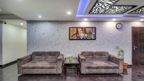 A lobby with two grey armchairs, a glass coffee table, a painting, a clock, and a door. - Treebo Trend Hotel NV (Narendranagar)