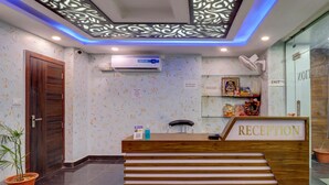 A reception area with a wooden desk, a reception sign, an air conditioning unit, and a wall with a decorative pattern. - Treebo Trend Hotel NV (Narendranagar)
