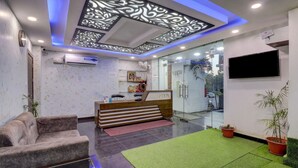 A reception area with a reception desk, a sofa, a glass door entrance, and a flat-screen TV mounted on the wall. - Treebo Trend Hotel NV (Narendranagar)
