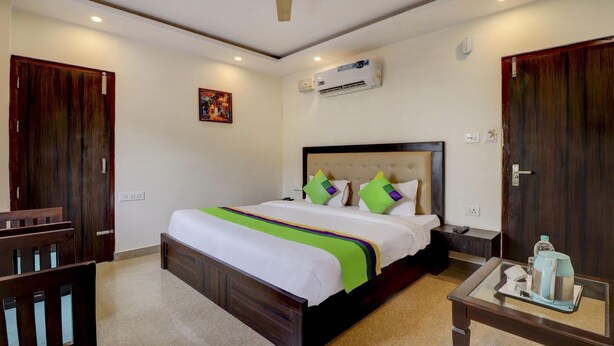 A hotel room with a large bed, a bedside table with a kettle, and a ceiling fan. - Treebo Trend Hotel NV (Narendranagar)
