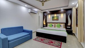 A bedroom with a bed, a blue sofa, a red and white patterned rug, and an air conditioning unit. - Treebo Trend Hotel NV (Narendranagar)