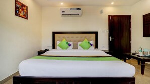 A hotel room with a bed, an air conditioner, a nightstand, a telephone, a door, and a painting on the wall. - Treebo Trend Hotel NV (Narendranagar)