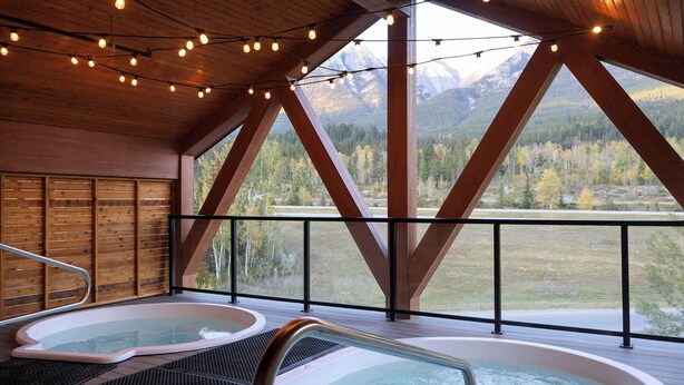Un espace avec un jacuzzi, doté d’un plafond en bois et de grandes fenêtres donnant sur un paysage montagneux.